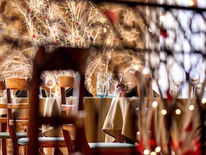 Un restaurante con mesas dispuestas para comer, sillas y un ambiente cálido con luces colgantes.