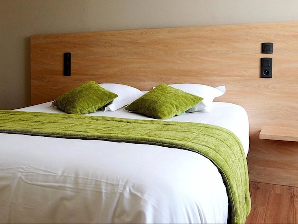 A neatly made bed with white linens and a green throw blanket, a wooden headboard, and two black bedside controls. - Hôtel du Grand Cerf (Ernee)