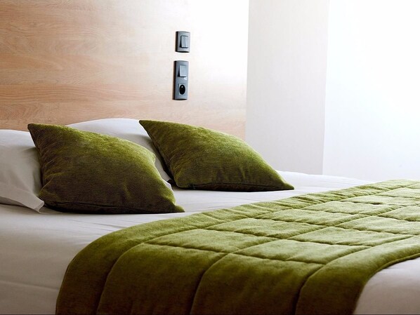Habitación de hotel con cama, dos almohadas verdes, una colcha verde acolchada y un interruptor de luz en la pared.
