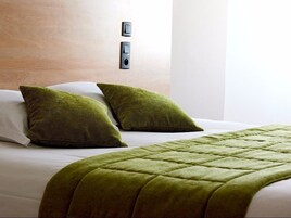 Habitación de hotel con cama, dos almohadas verdes, una colcha verde acolchada y un interruptor de luz en la pared.