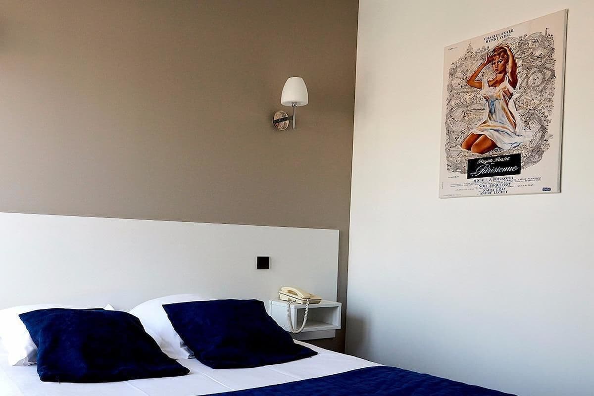 A hotel room with a bed, two pillows, a bedside table with a lamp, and a poster on the wall.