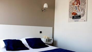 A hotel room with a bed, two pillows, a bedside table with a lamp, and a poster on the wall.