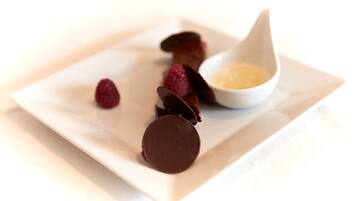 A dessert plate with chocolate pieces and raspberries, and a small bowl of cream.
