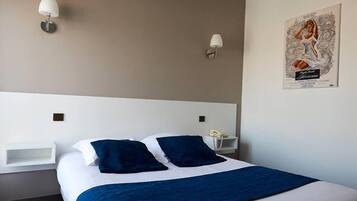 A hotel room with a large bed, two bedside tables, a nightstand with a lamp, and a poster on the wall.