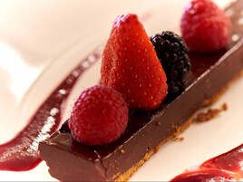 Un postre con fresas, frambuesas y moras sobre una base de chocolate.