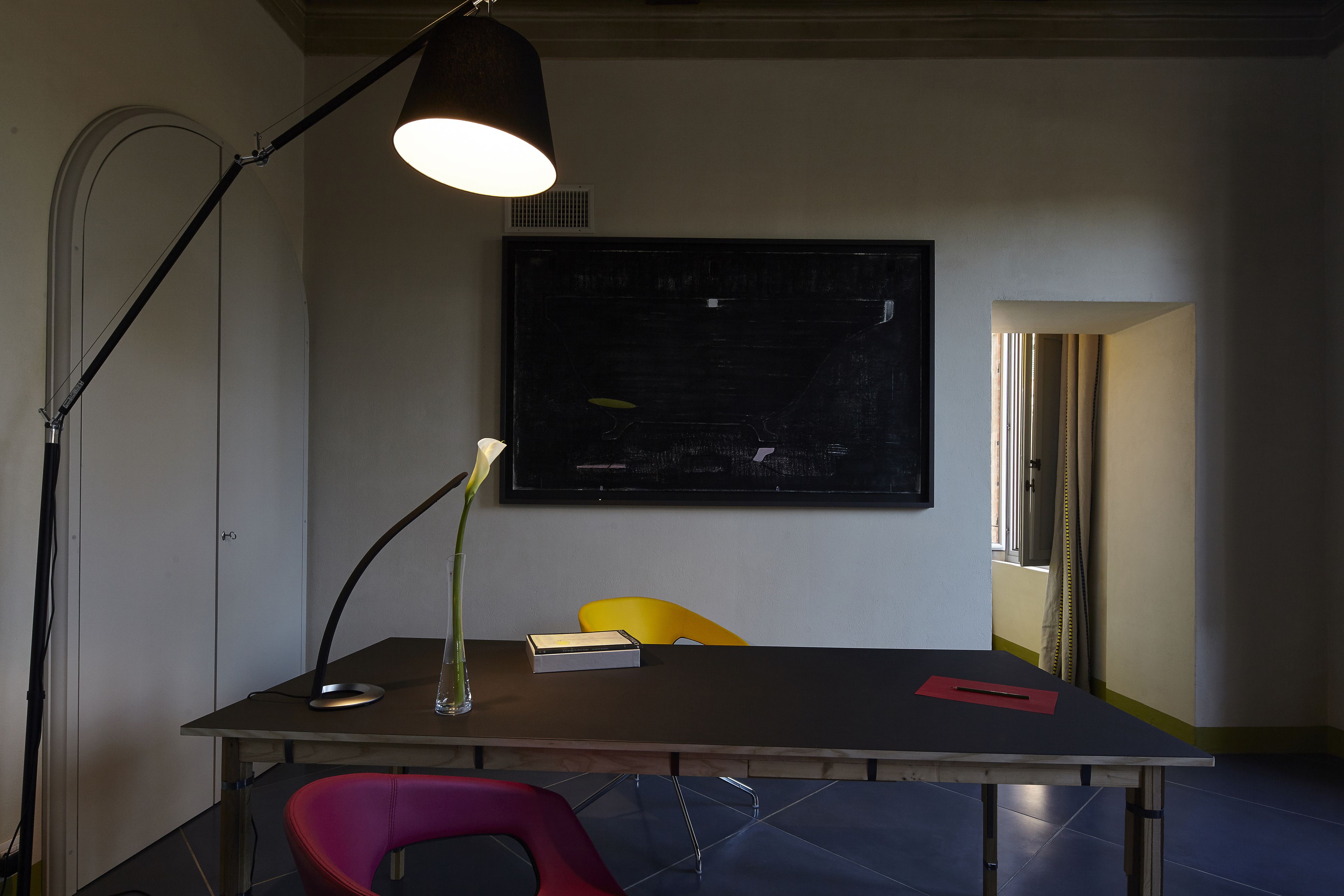 Una stanza con una scrivania, una sedia, una lampada e un quadro appeso al muro.