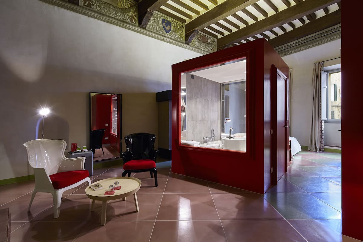 Habitación de hotel con una pared de acento roja, una mesa redonda con cojín rojo, una silla blanca y una silla negra.
