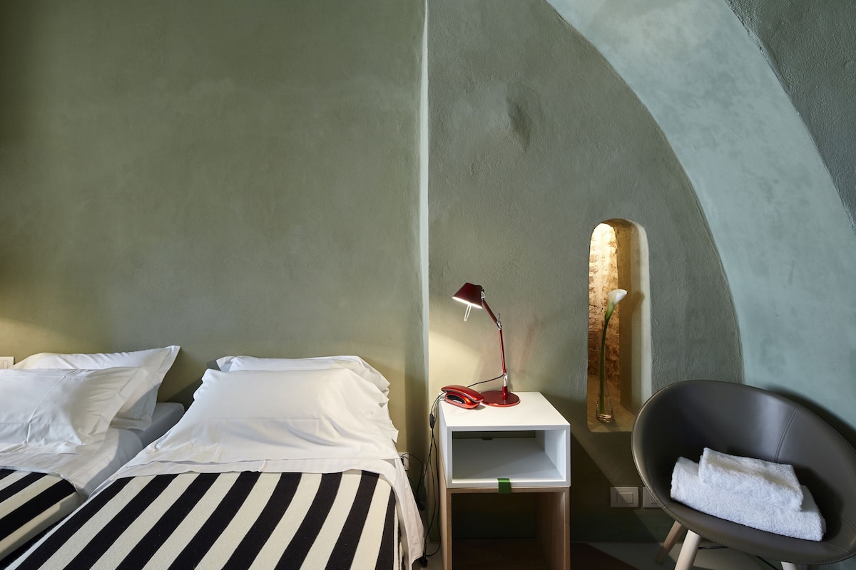 Habitación de hotel con dos camas, una mesita de noche con lámpara, una silla con toalla y un aplique de pared.