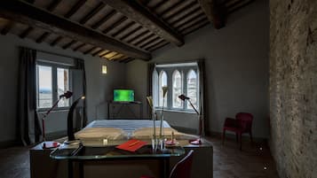 A room with a glass desk, two red chairs, a television, and a view through arched windows.