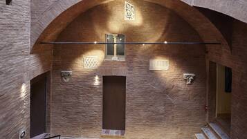 A stone-walled interior with a central door, a staircase, and a decorative light fixture.