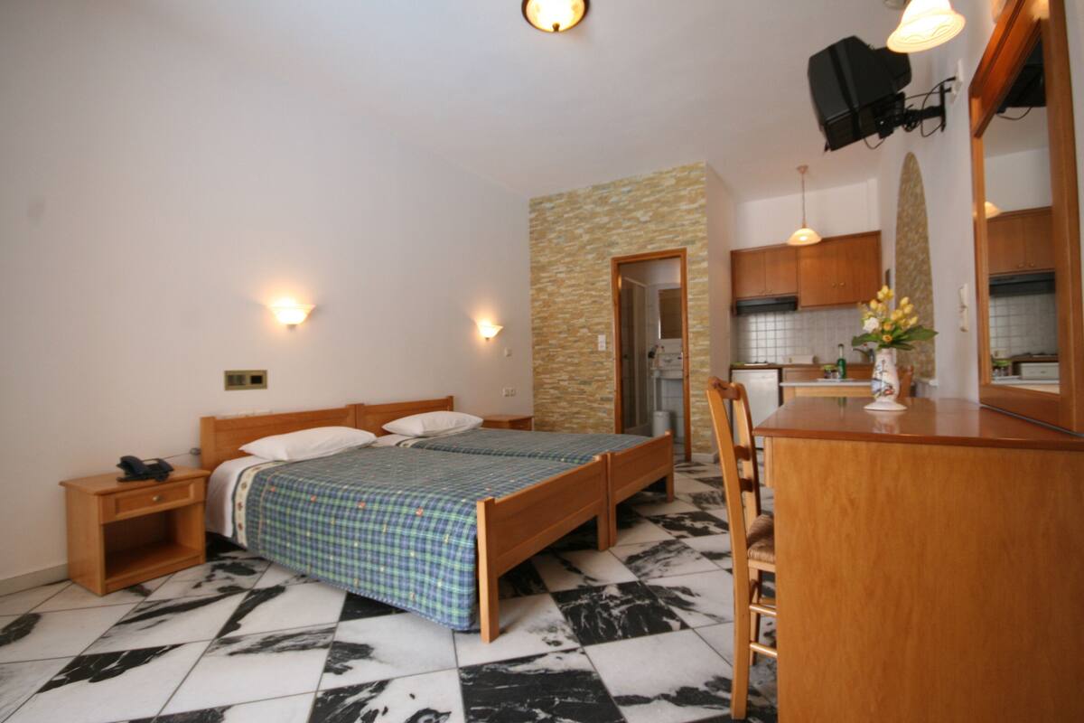 Une chambre à coucher avec un lit, une table de chevet et un petit bureau avec une chaise. Un miroir est placé au-dessus du bureau et un mur en pierre se trouve au fond de la pièce.