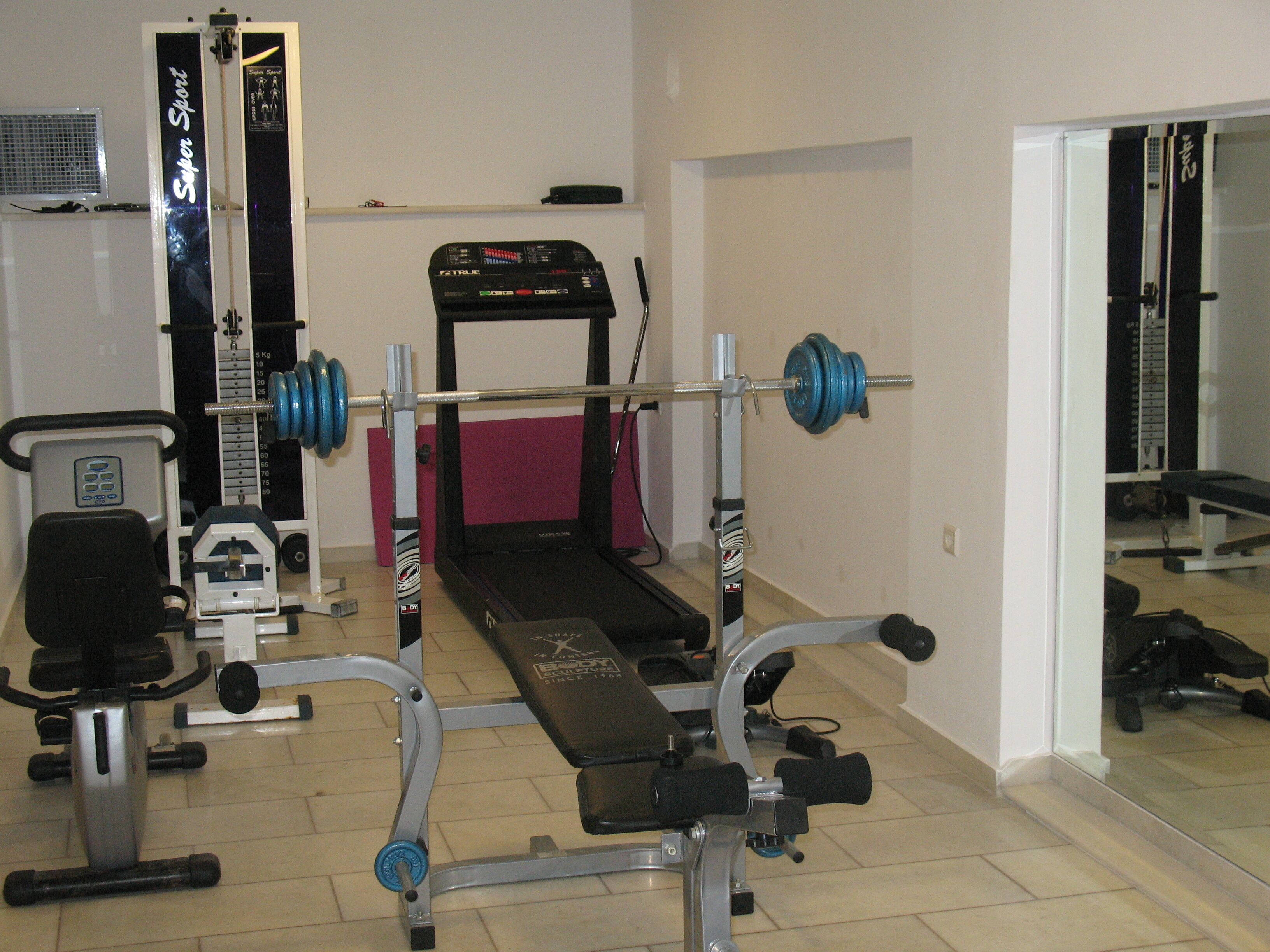 Una palestra in casa con una panca per i pesi, un tapis roulant e una rastrelliera per attrezzi.