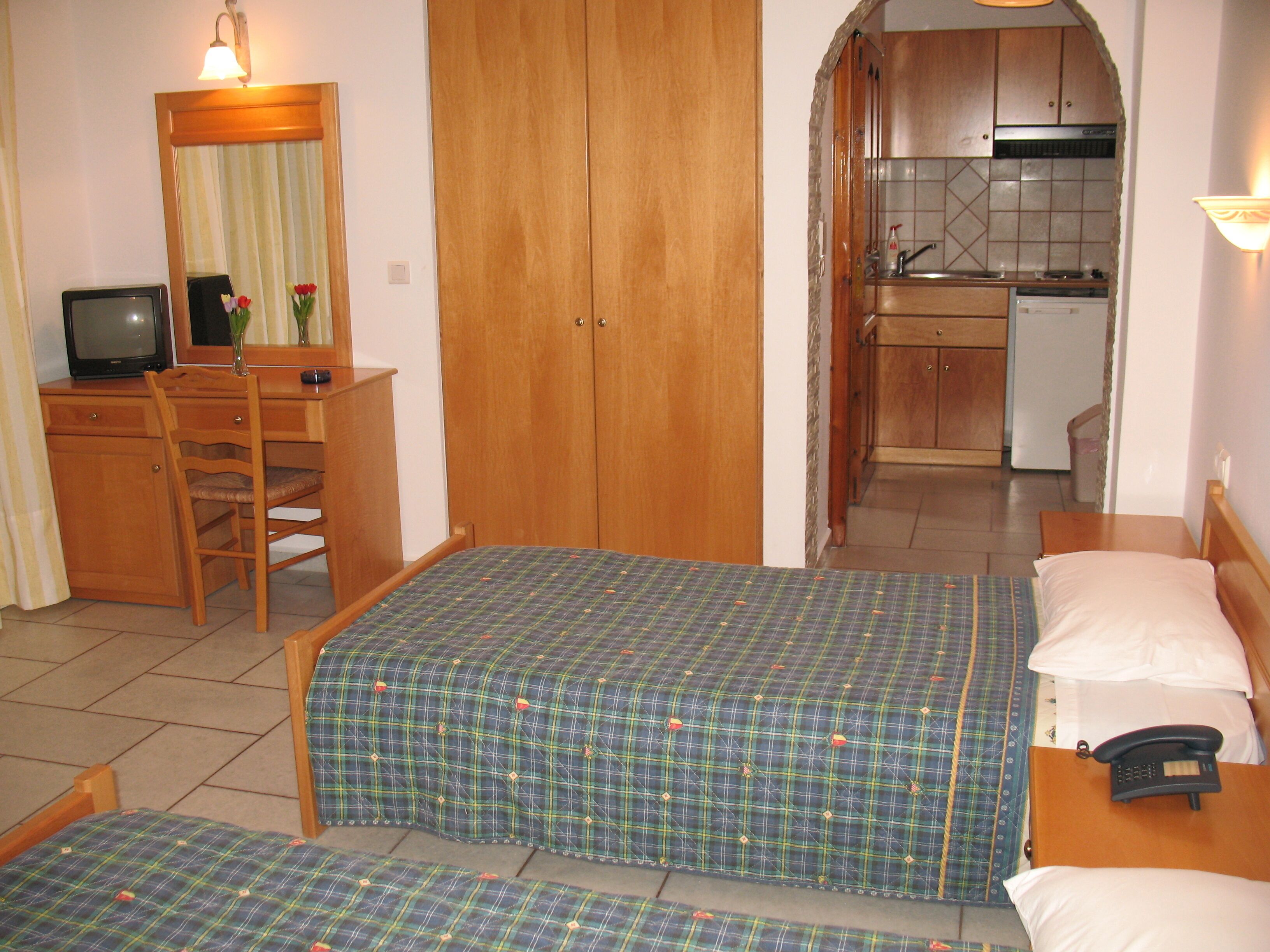 Une chambre d’hôtel avec deux lits, un bureau avec un ordinateur, un miroir et une kitchenette.