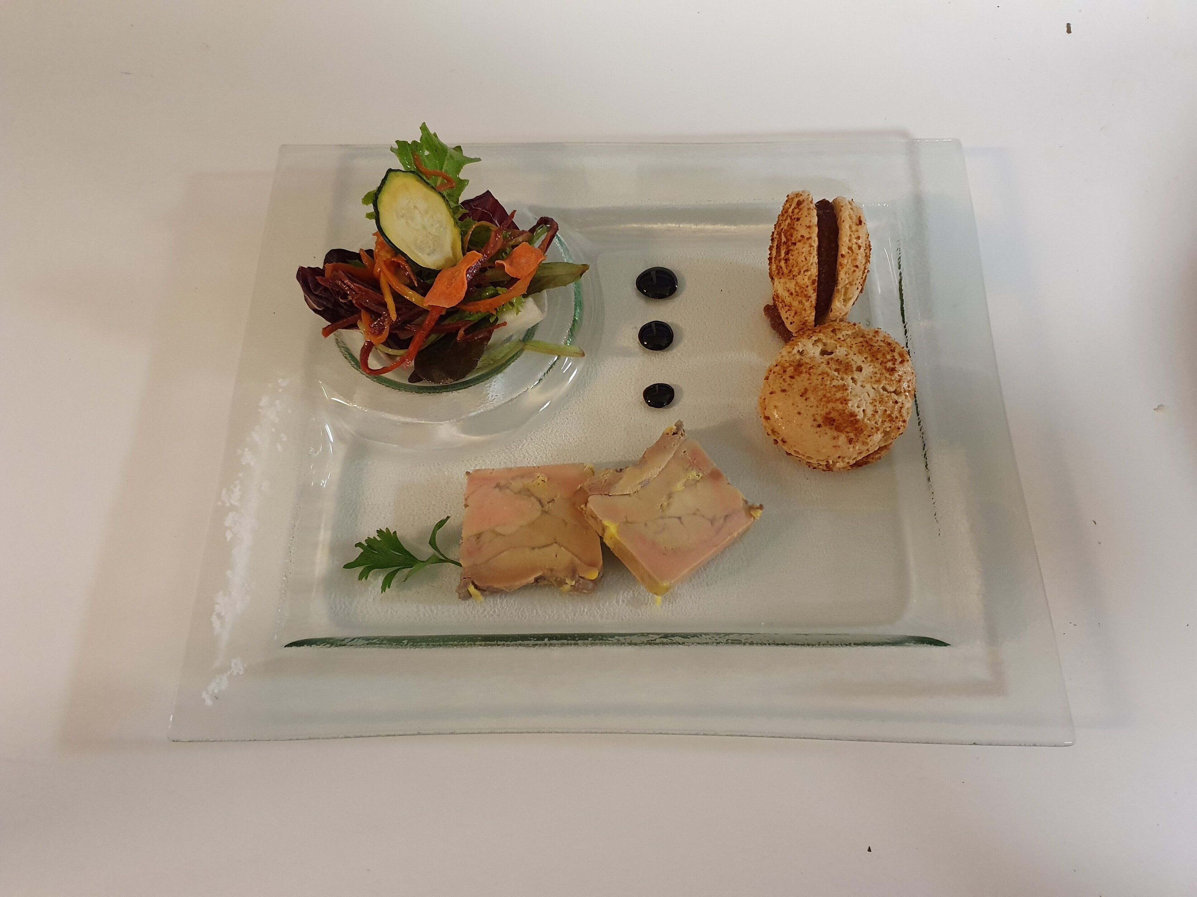 A clear glass plate with a salad, two pieces of toast, and a slice of meat.