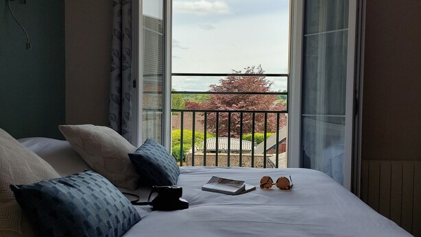 A hotel room with a large bed, a view of a balcony with a railing, and a window with curtains. - Hôtel le Relais de l'Abbaye (Saint-Evroult-Notre-Dame-du-Bois)