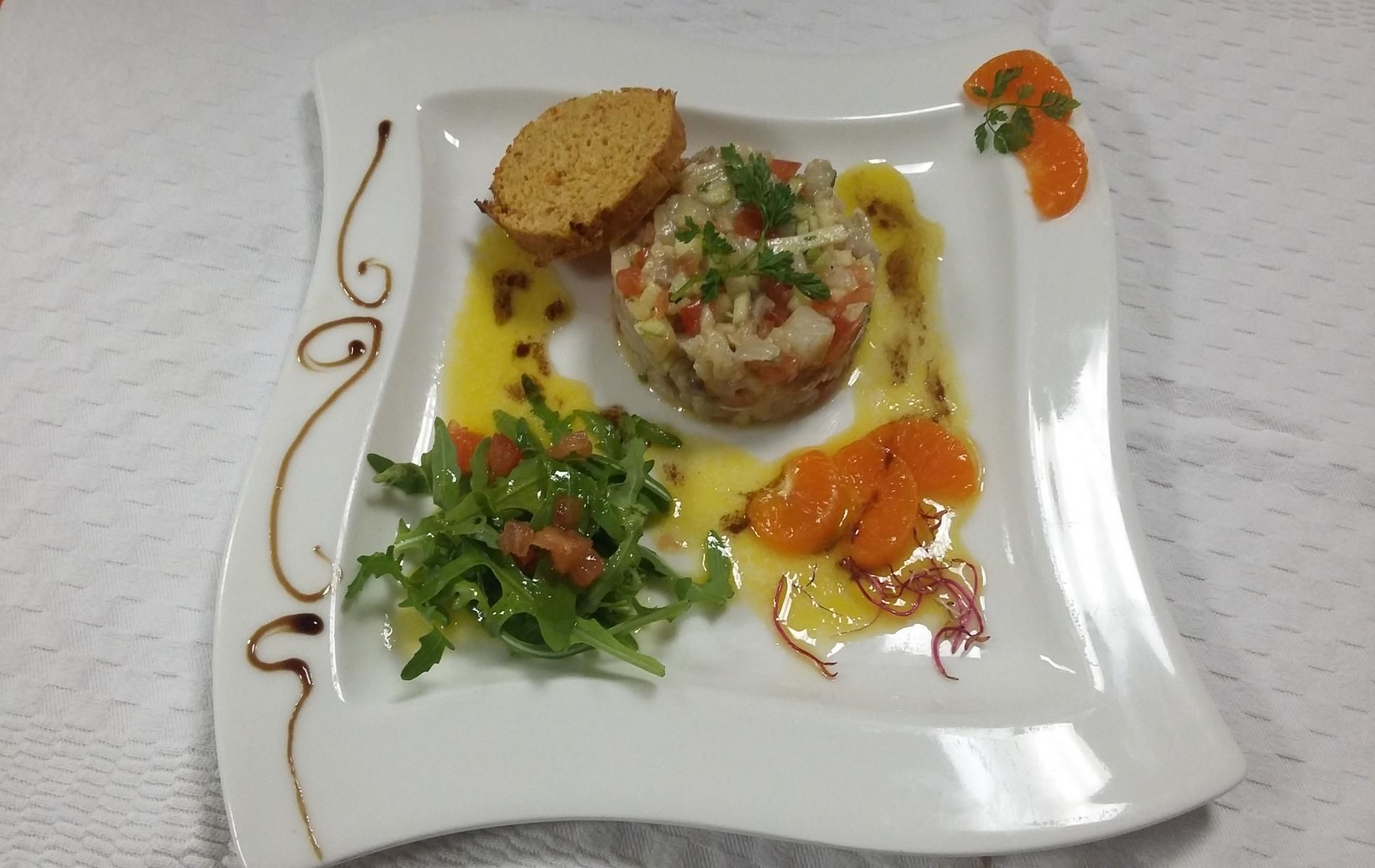 A square white plate with a food dish, a piece of bread, and some greens.