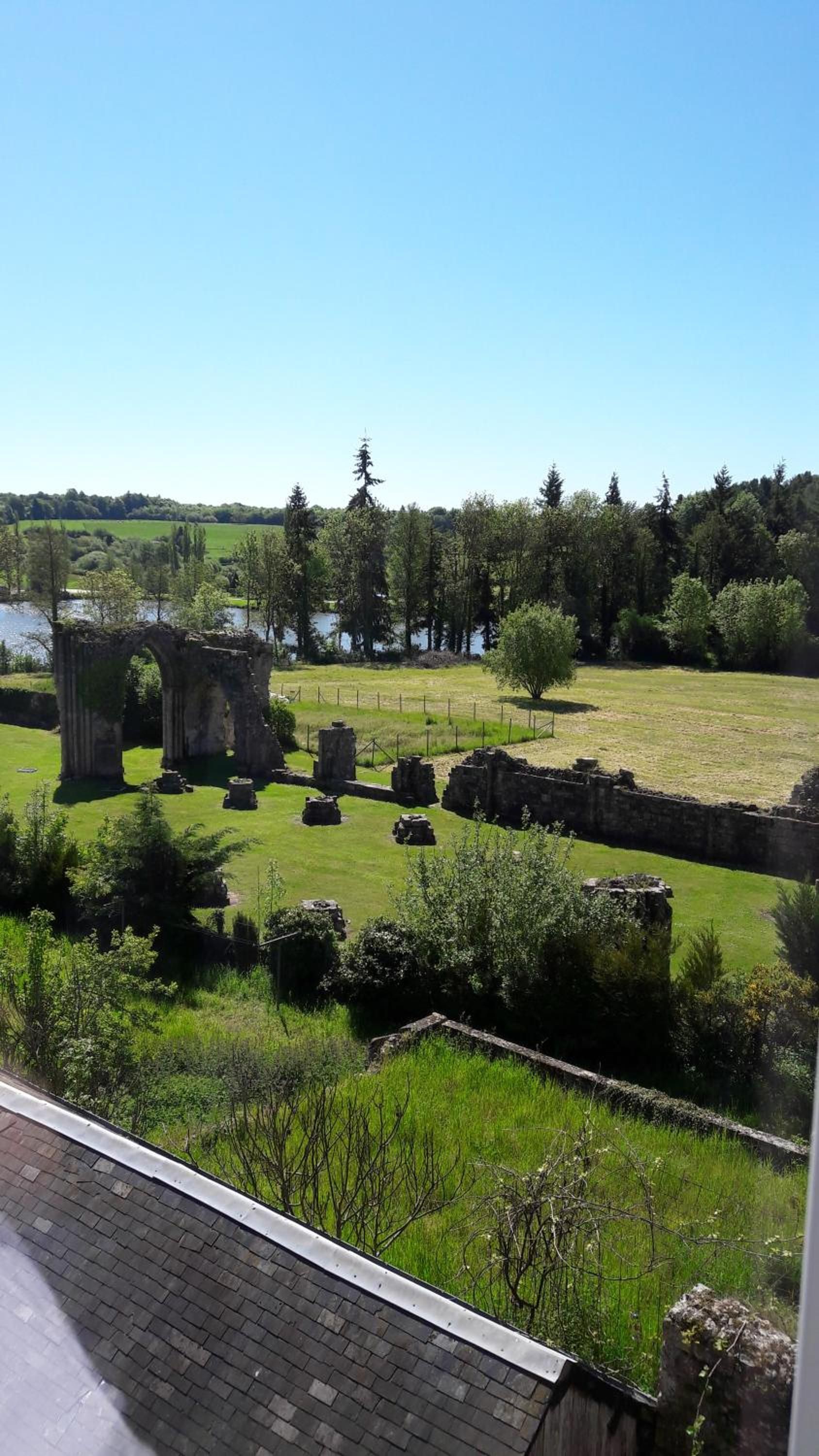 Vista de un sitio histórico con ruinas, un campo cubierto de césped y una masa de agua al fondo.