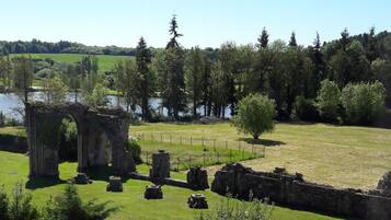 Vista de un sitio histórico con ruinas, un campo cubierto de césped y una masa de agua al fondo.