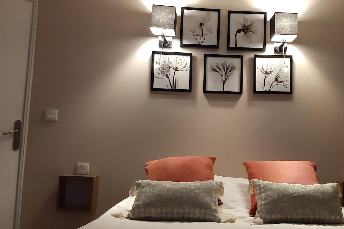Un lit bien fait avec deux oreillers, un mur orné de tableaux encadrés et deux lampes de chevet.
