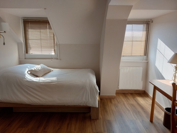 Un dormitorio con cama, radiador, ventana y escritorio.