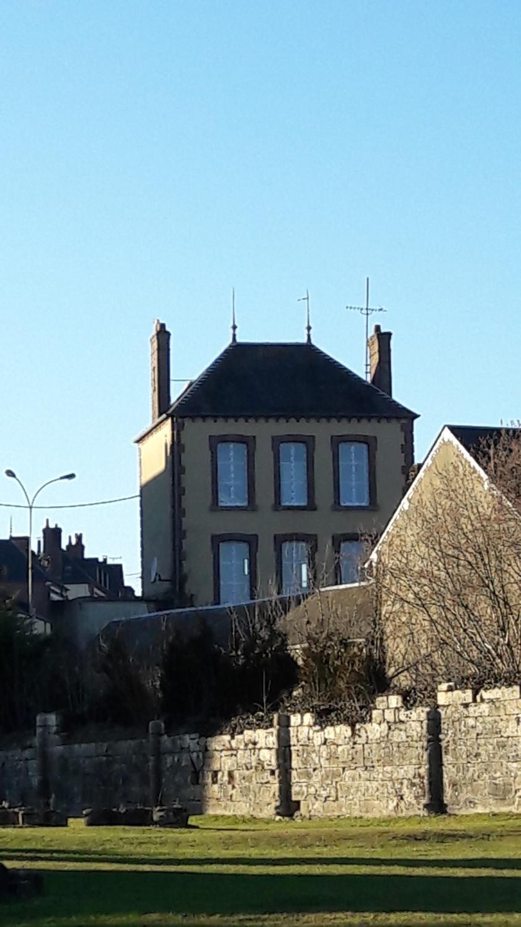 Un edificio de dos pisos con fachada simétrica, múltiples ventanas y una chimenea central.