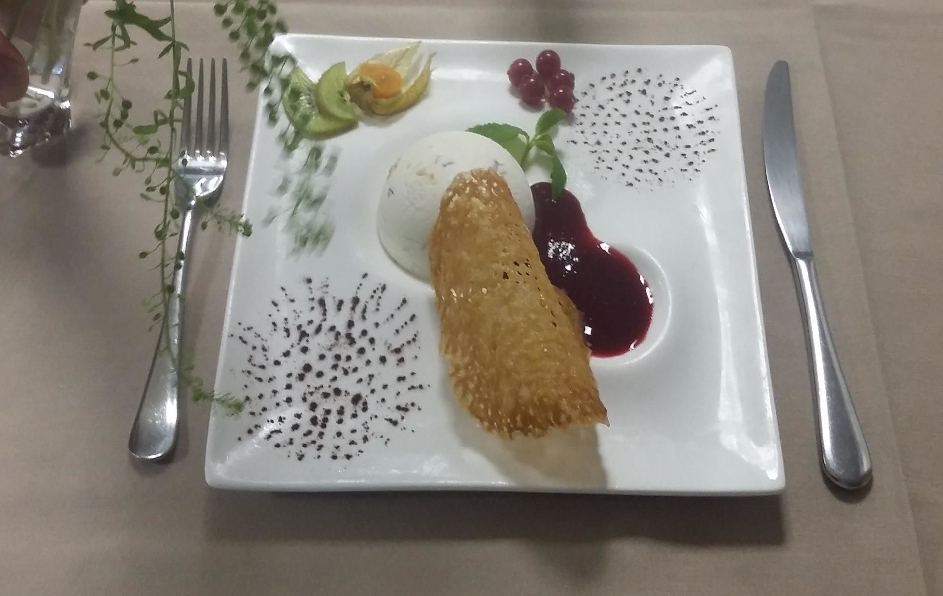 Un plato blanco cuadrado con un alimento frito, una cucharada de crema y salsa de frutos rojos.