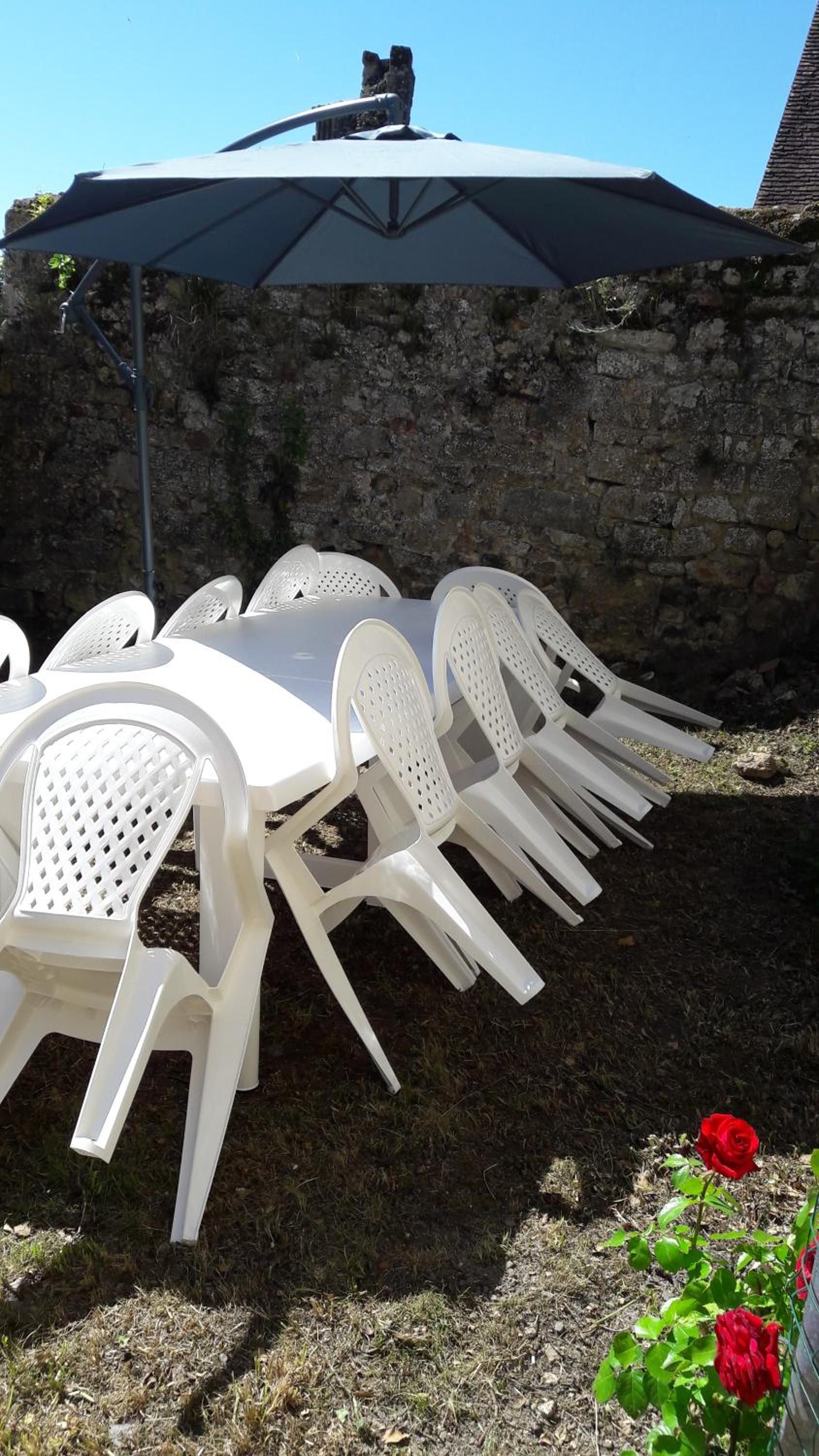 Outdoor patio furniture arranged around a table, with a stone wall and a clear sky in the background.