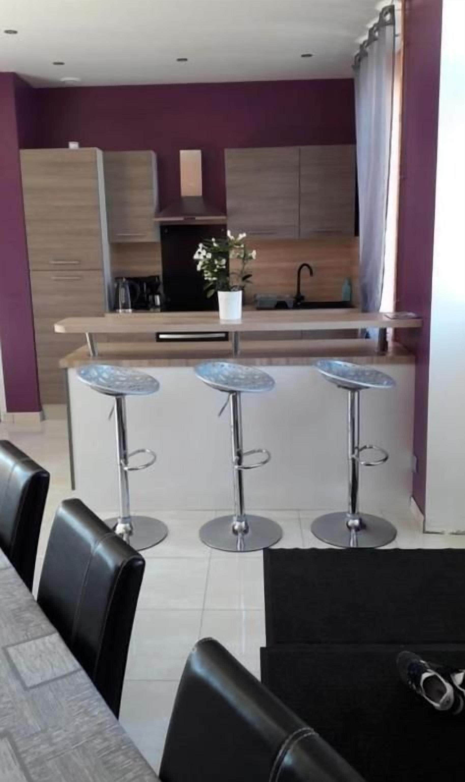 Een moderne keuken met een centraal eiland, barkrukken en een eethoek met stoelen.