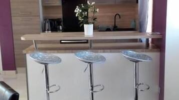Een moderne keuken met een centraal eiland, barkrukken en een eethoek met stoelen.