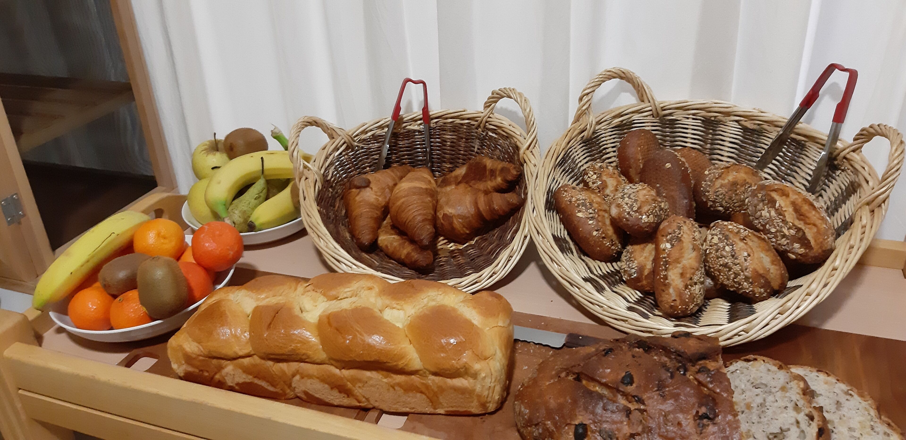 A breakfast buffet with bread, pastries, and fruits.