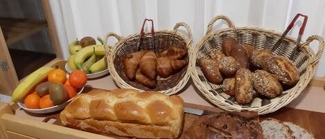 A breakfast buffet with bread, pastries, and fruits.