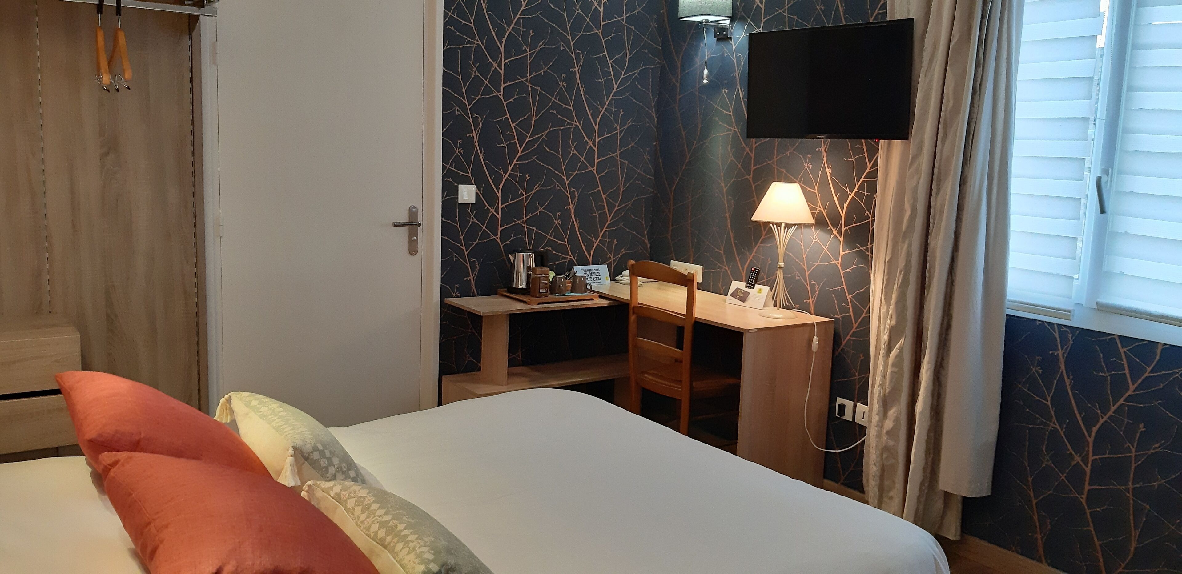 Una habitación de hotel con una cama, un escritorio con silla, un televisor montado en la pared y una ventana con cortinas.
