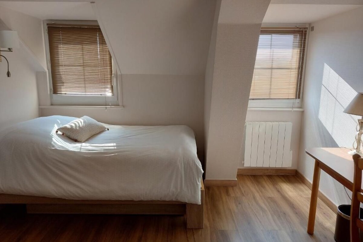 A bedroom with a bed, a radiator, and a window with blinds.