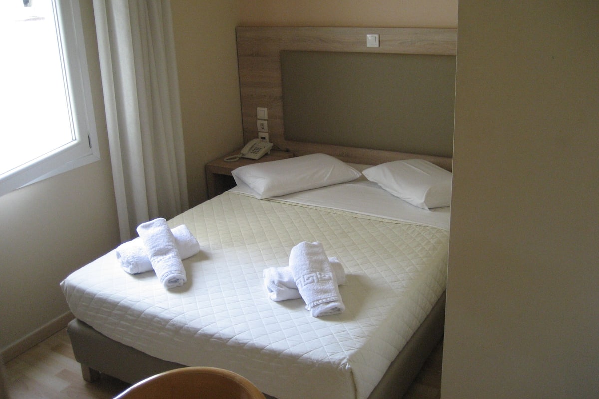 Hotellihuone, jossa on sänky, yöpöytä, jossa on puhelin, ja ikkuna, jossa on verhot.