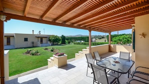 Un porxo cobert amb una taula i cadires, un jardí i vista a una zona residencial.