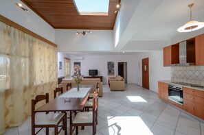 A spacious living area with a dining table, sofas, and a kitchen with wooden cabinets and a built-in oven.
