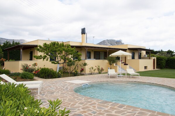 A modern house with a swimming pool, outdoor seating, and a mountain backdrop.
