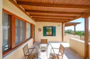 A covered outdoor patio with a table and chairs, large windows, and a view of the landscape.