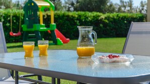 Taula amb gerro de suc de taronja i dues copes de suc de taronja, plat amb menjar, i un parc infantil al fons.