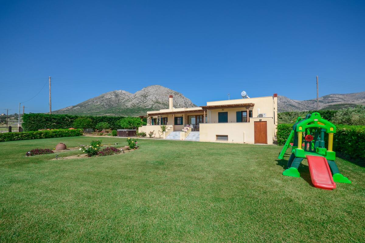 A house with a front yard, a play structure, and mountains in the background.