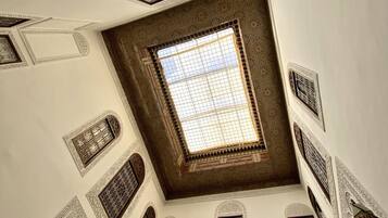 Una habitación con techos altos y detalles arquitectónicos elaborados, incluyendo celosías ornamentales en las ventanas y diseños geométricos en las paredes.
