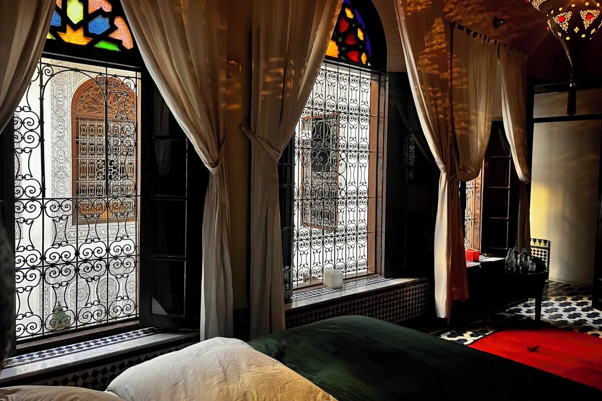 A room with a bed, a window with ornate ironwork, and a chandelier.