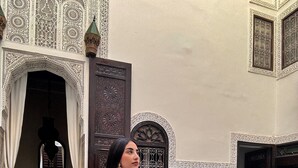 A woman in a blue dress standing in a room with a checkered floor, ornate doors, and a table set for dining. - Riad Tizwa Fes (Fes)