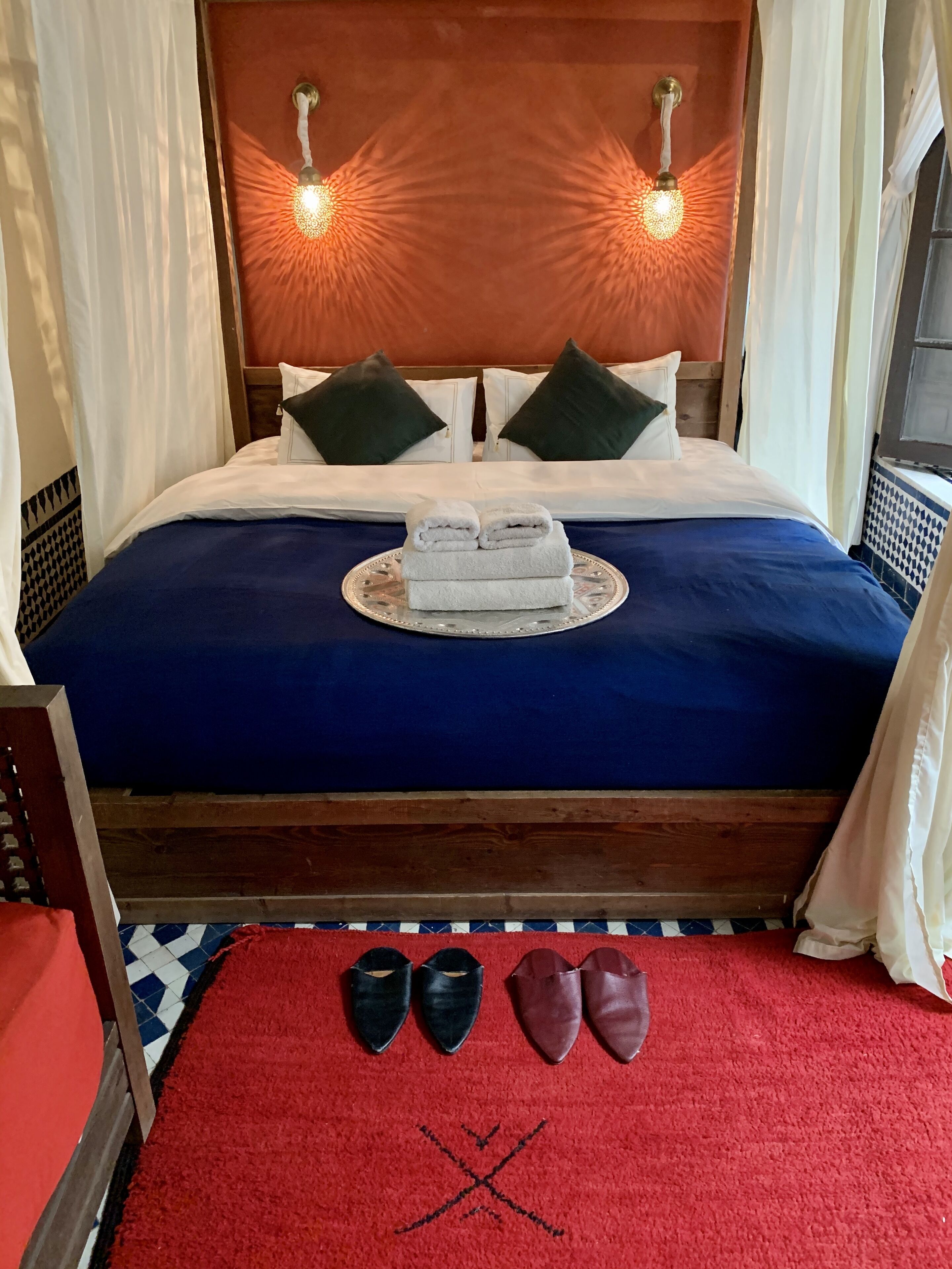 A neatly made bed with a blue bedspread, two pillows, and a pair of folded towels on a decorative tray.