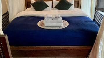 A neatly made bed with a blue bedspread, two pillows, and a pair of folded towels on a decorative tray.