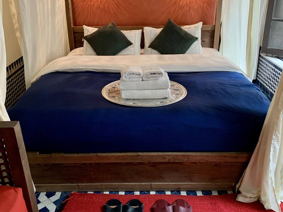 A neatly made bed with a blue bedspread, two pillows, and a pair of folded towels on a decorative tray.