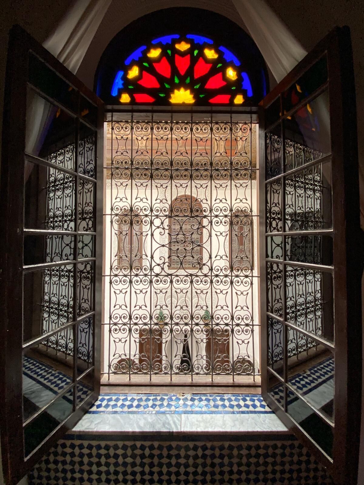 A room with a patterned floor, a stained glass window, and a view of a building through a decorative metal screen.