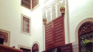 An interior with ornate wooden doors, a checkered floor, and a white chair. - Riad Tizwa Fes (Fes)