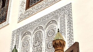 A building facade with intricate white lattice window designs and detailed wooden door frames. - Riad Tizwa Fes (Fes)