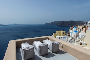 Une terrasse agrémentée de coussins blancs, offrant une vue sur la mer et un village côtier.